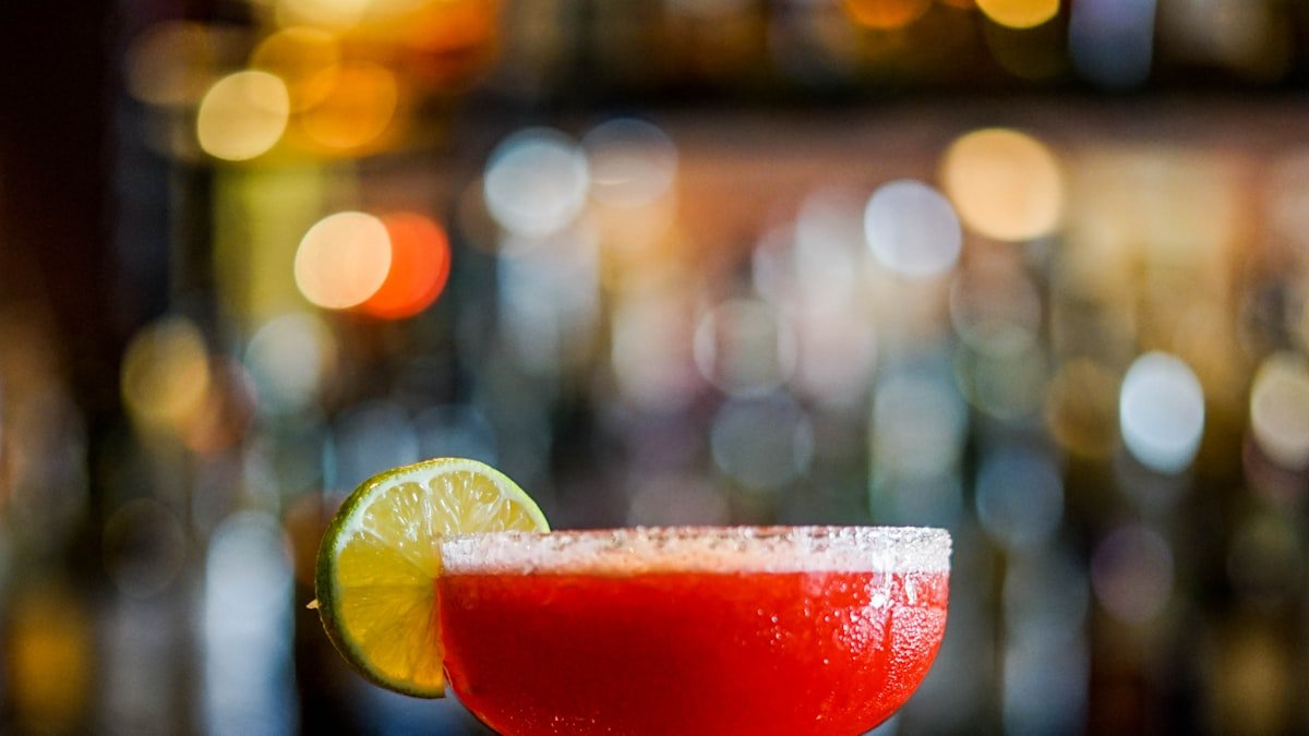 Classic margarita cocktail with lime at a bar, warm ambient lights in the background