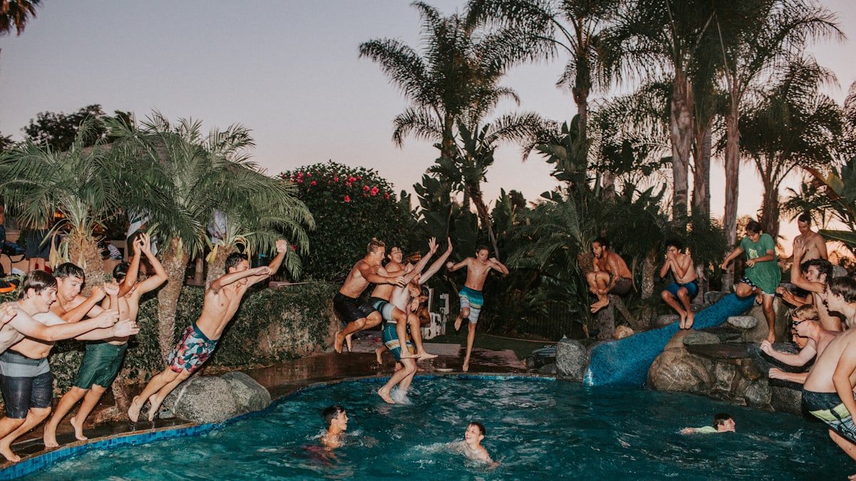 Guests jumping into a resort pool at dusk, lively nightlife atmosphere