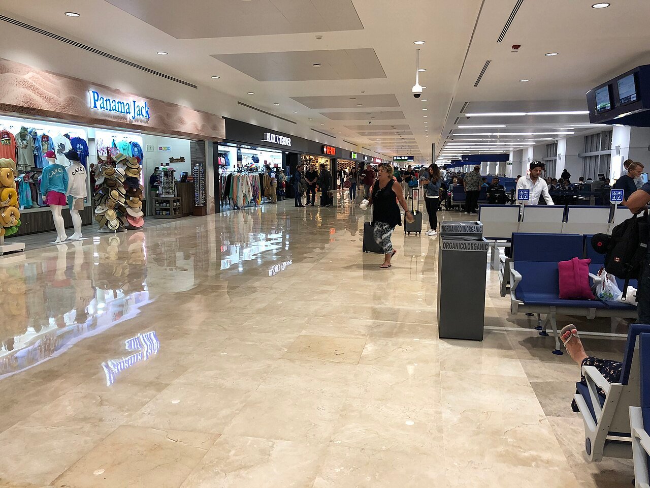 Pasajeros con maletas caminando por el pasillo comercial del aeropuerto de Cancún