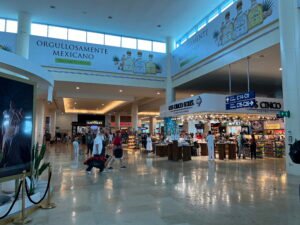 Interior corridor at Cancún International Airport with travelers walking past shops, 2024