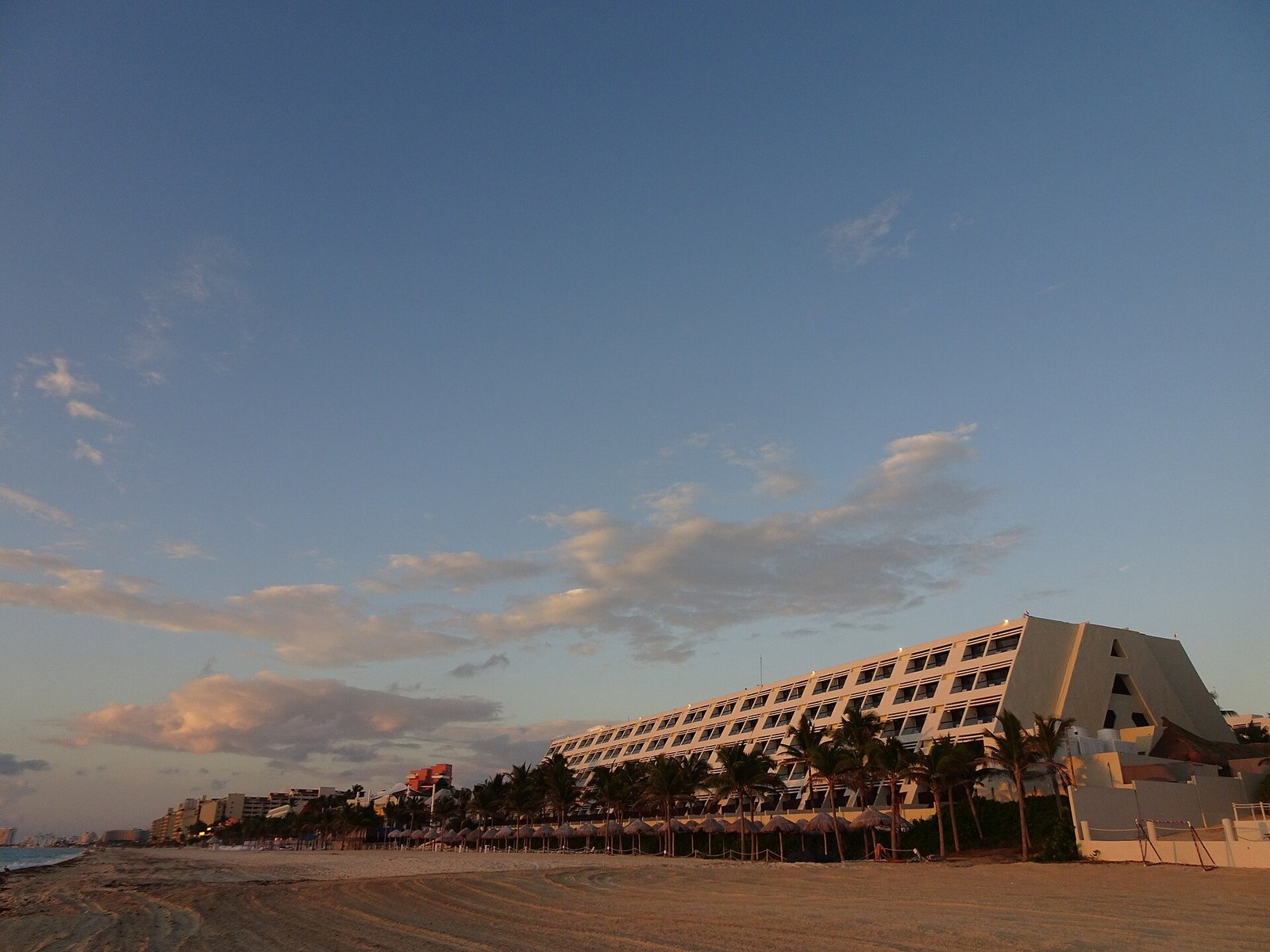 Empty stretch of beach at dusk in front of a pyramid-shaped hotel in Cancun