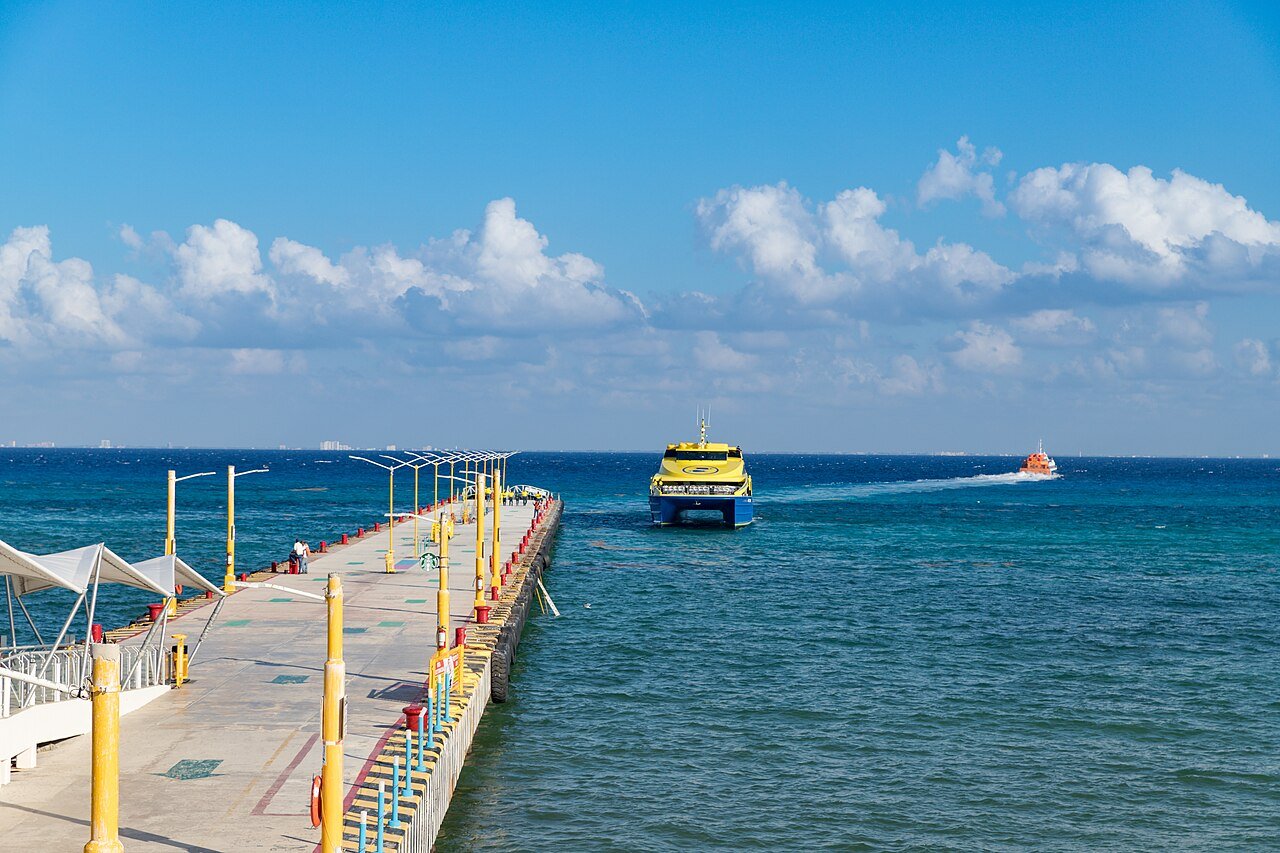Muelle de ferry en Playa del Carmen con una embarcación saliendo hacia Cozumel