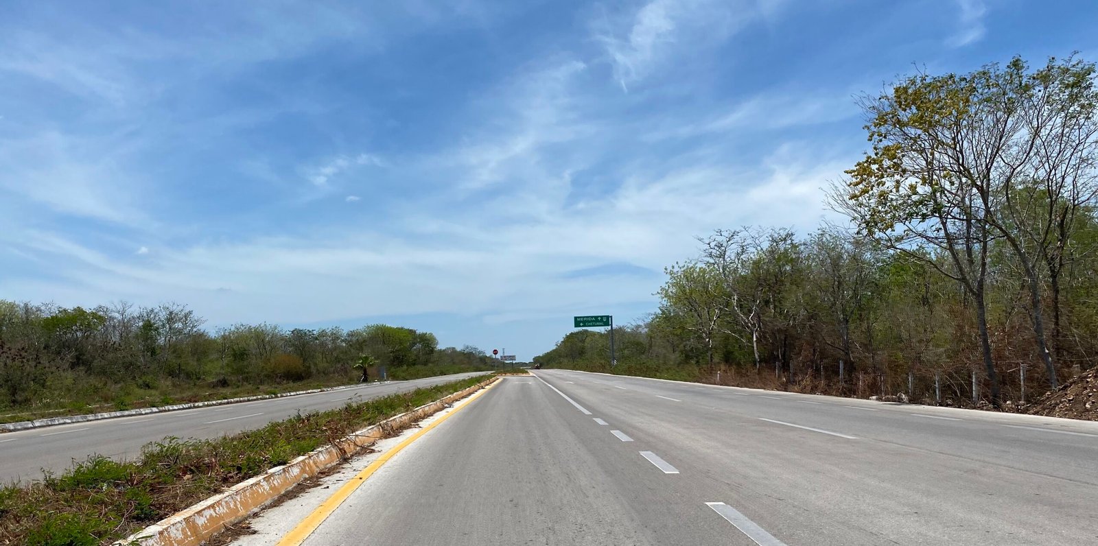 Empty two-lane highway through the Yucatan countryside with a green route sign