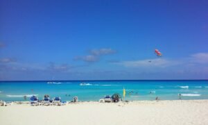 White sand beach and turquoise water in Cancun with a parasail in the sky