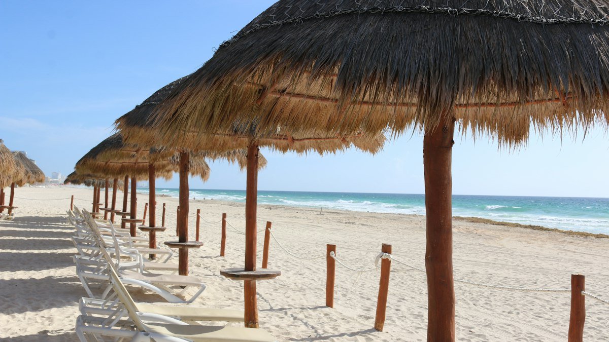 Rows of wooden beach umbrellas on a sunny beach in Cancún