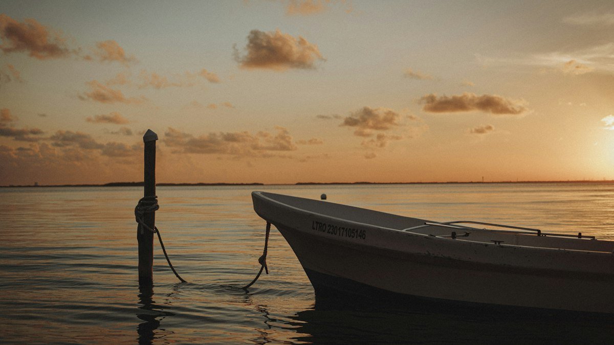Small boat tied to a pole in calm water off Cancún as the sun goes down