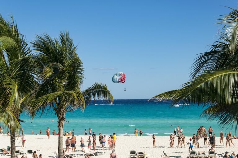 Sunny Cancún beach with palm trees, swimmers, turquoise sea and a parasail overhead