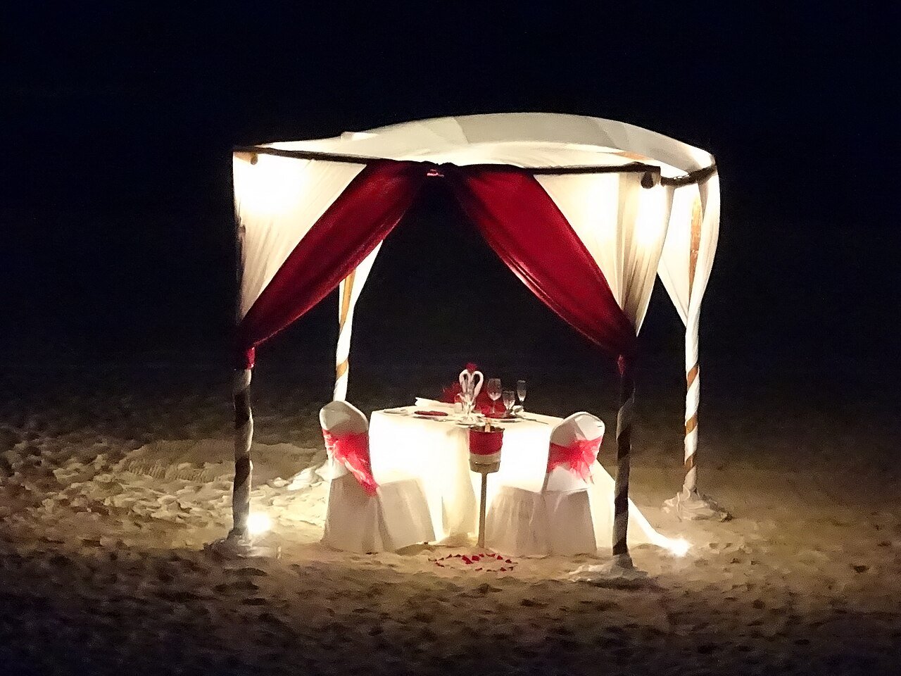 Mesa montada bajo un dosel con cortinas para una cena en la arena de una playa de Cancún de noche