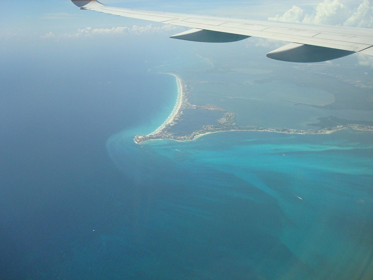 Airplane wing over the turquoise Cancún coastline after takeoff