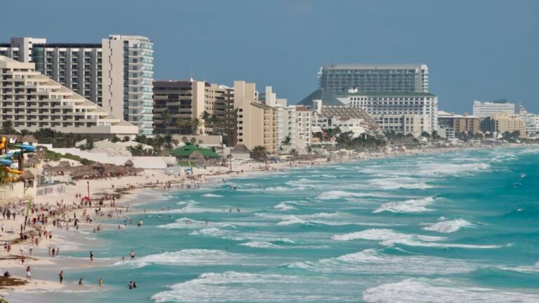 Row of hotels along a busy beach with turquoise surf in the Cancun Hotel Zone