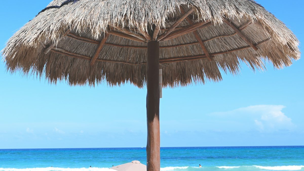 Straw umbrella on the sand with waves at Punta Cancún, Cancún Hotel Zone