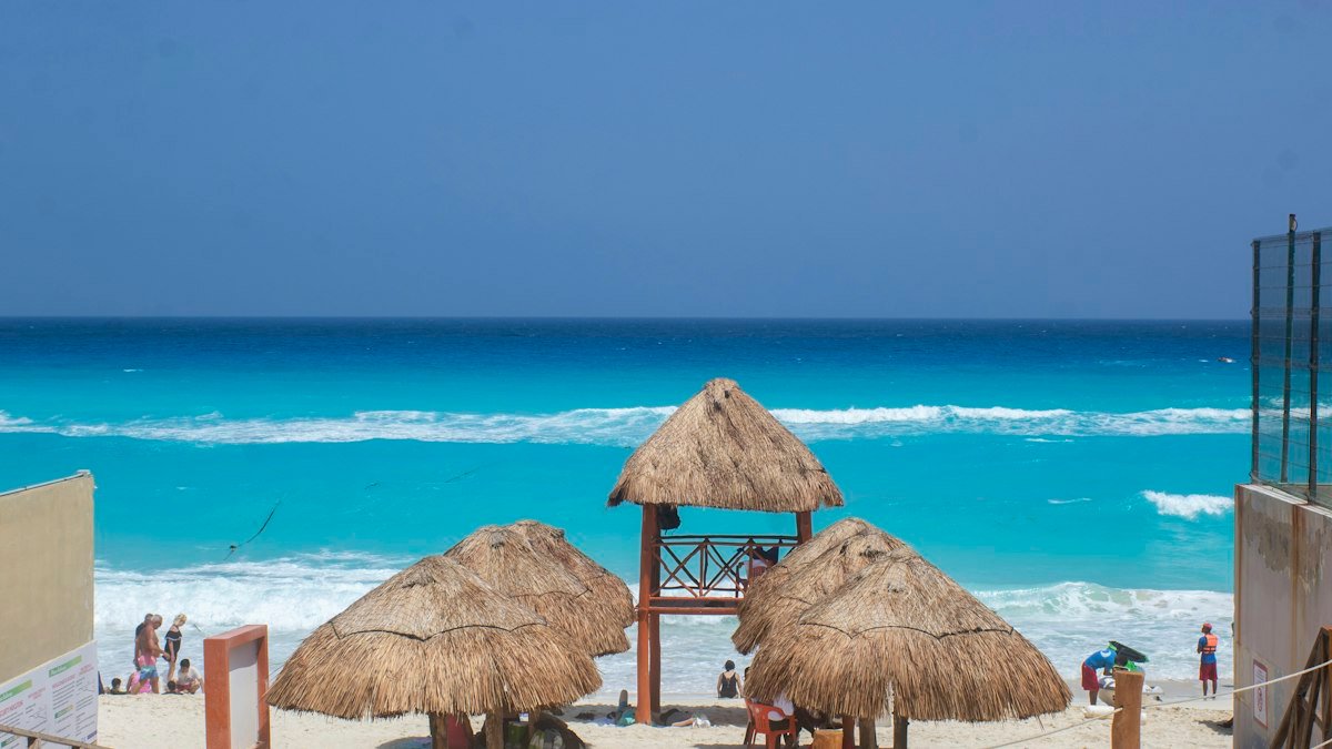 Straw palapa umbrellas lined up on a beach in Cancún