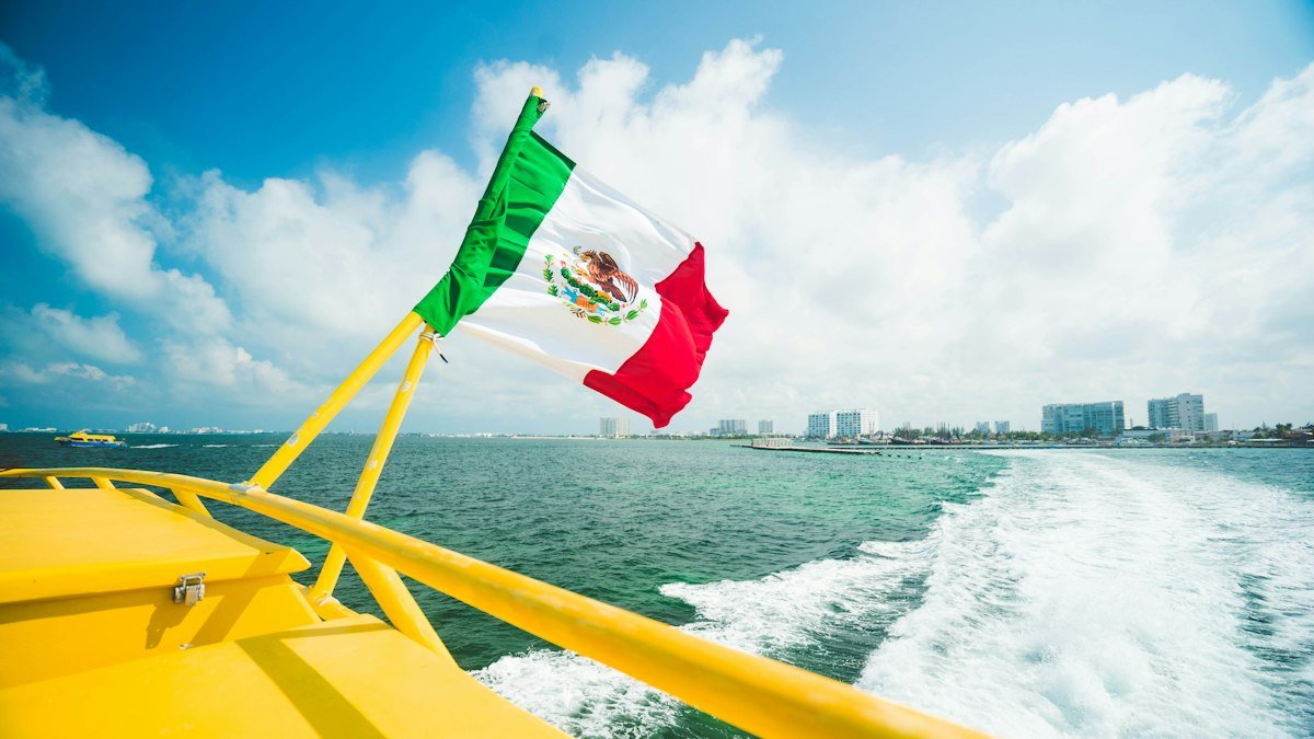 Mexican flag flying on a yellow boat on the water in Cancún