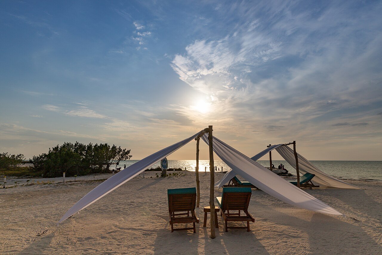 Canvas shade sails and chairs on the sand at Isla Holbox with the sun low over the water
