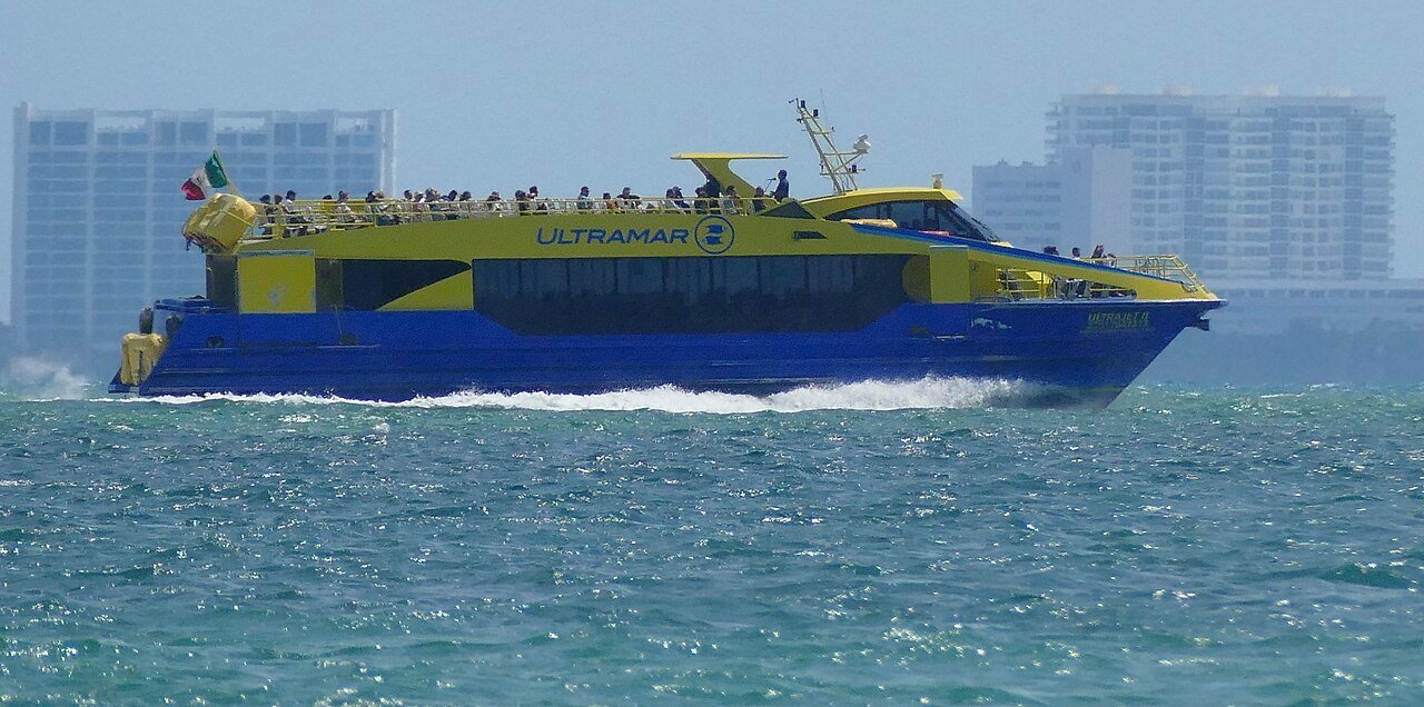 Yellow and blue fast ferry to Isla Mujeres crossing the bay, seen from Playa del Niño in Cancun