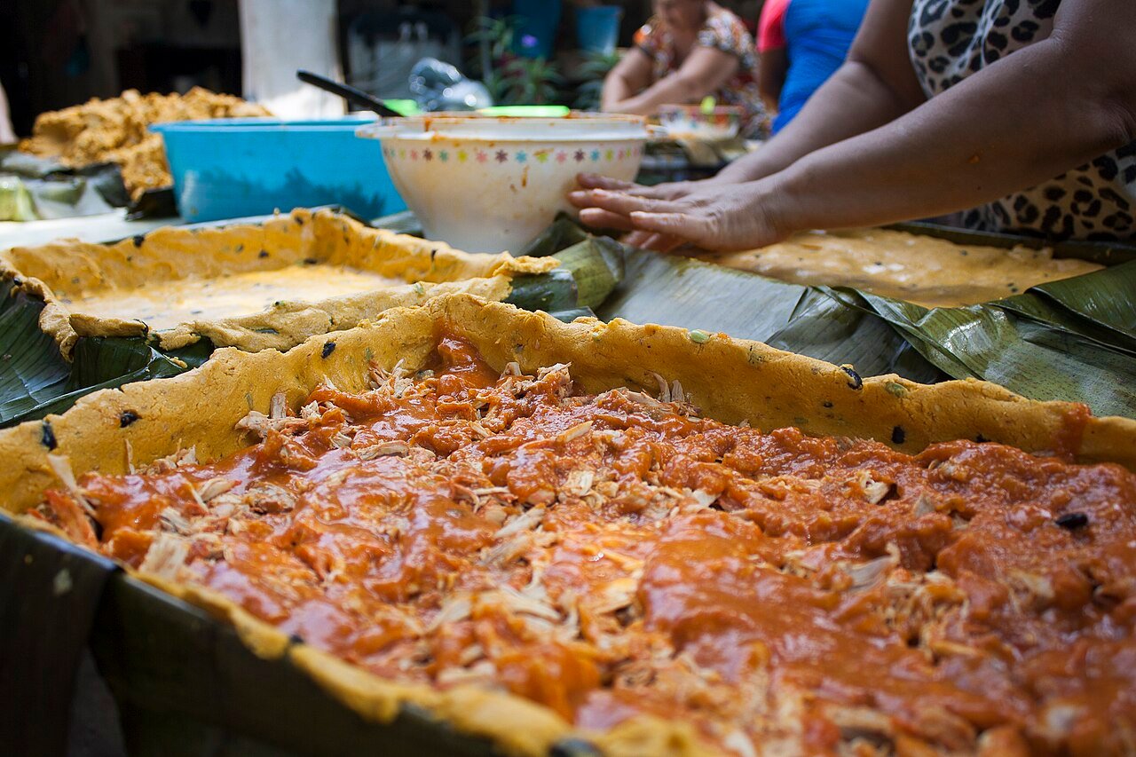 Manos preparando mucbipollo, el tamal grande yucateco de Día de Muertos, en moldes con hoja de plátano
