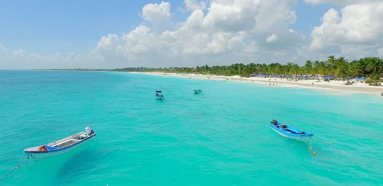 Small boats on turquoise water off a white sand beach in Tulum, Mexico