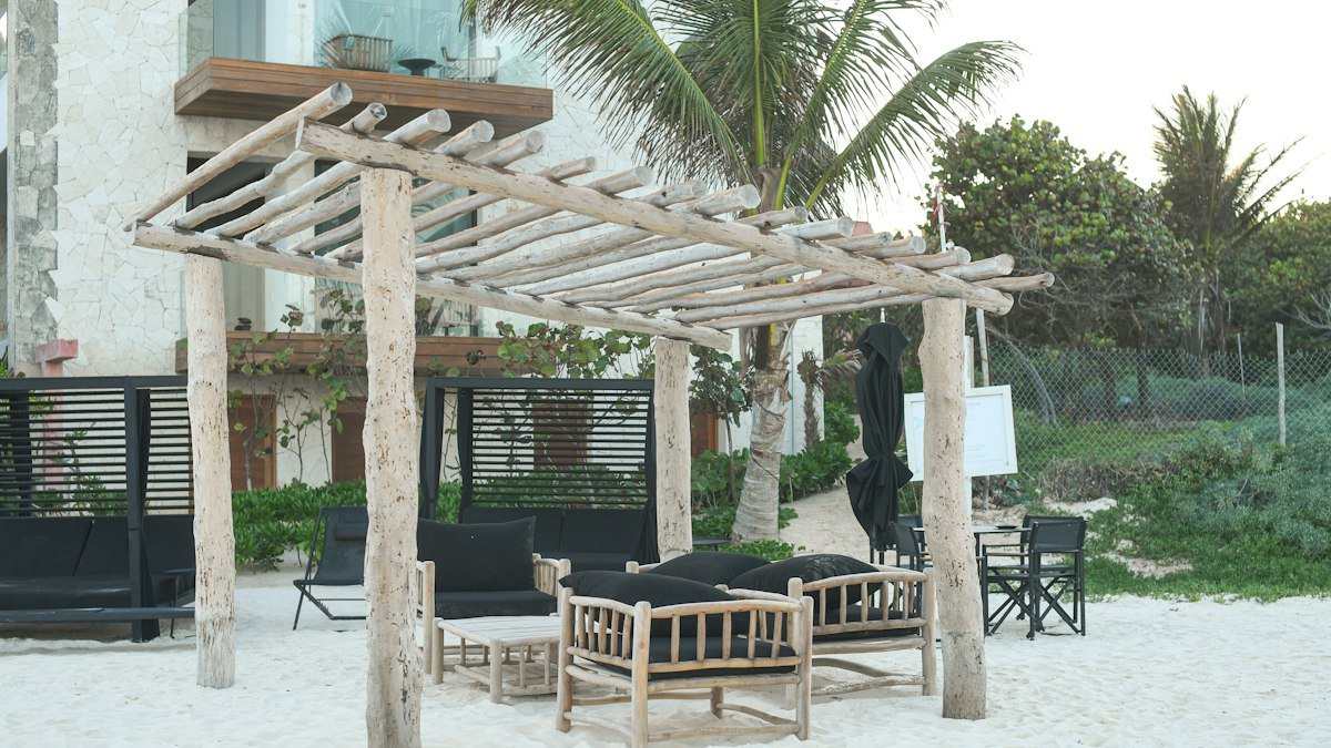 Beach lounge area with a rustic wooden pergola and seating on the sand in Tulum